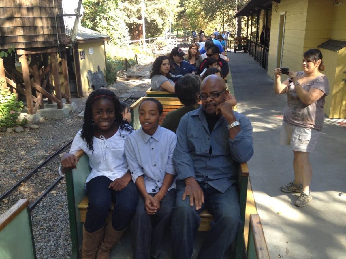Alex riding a miniature train with two kids, family outing