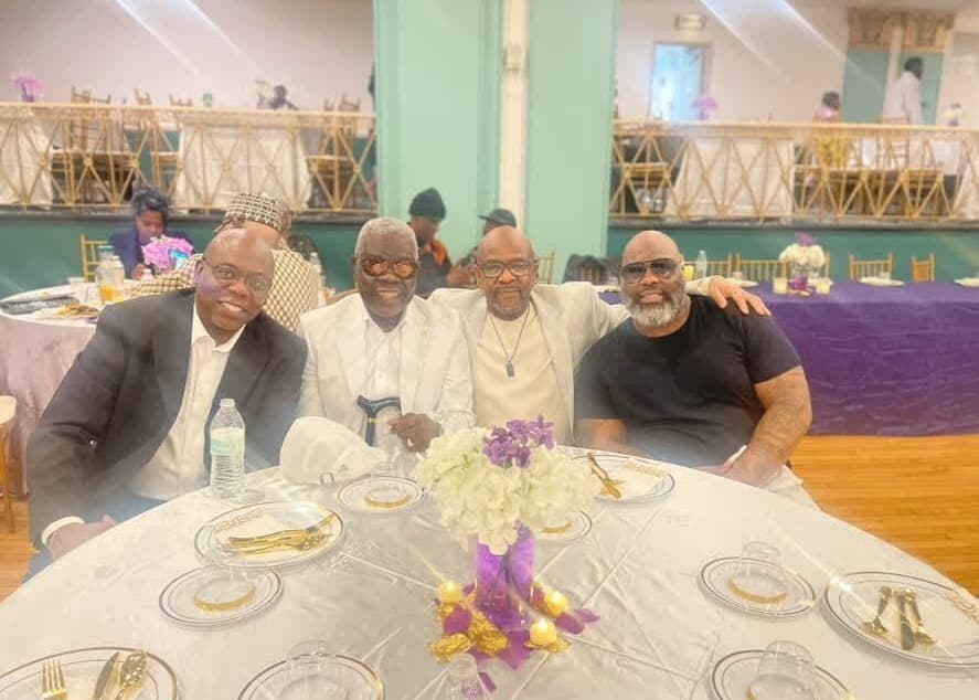 Four friends at a formal banquet table, arms around each other