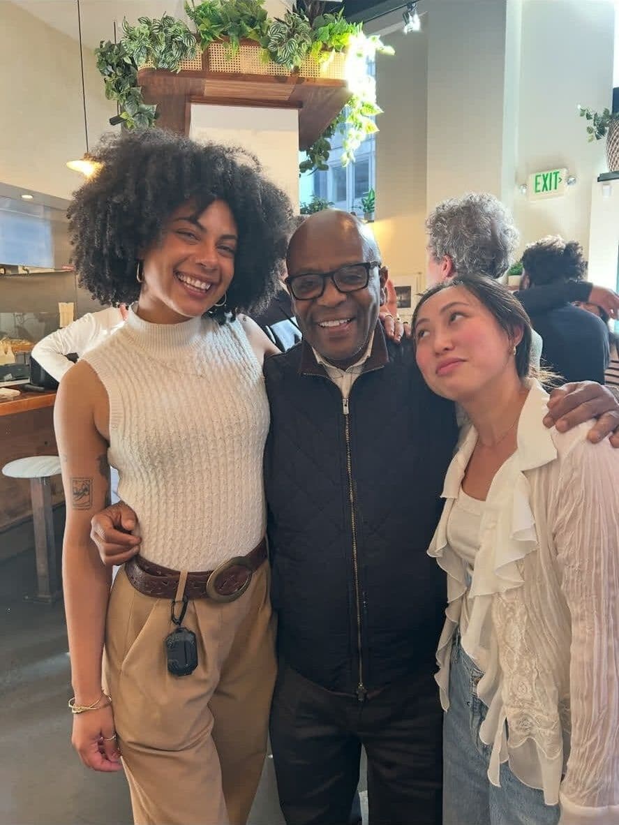 Alex with two young women at a cafe, arms around them