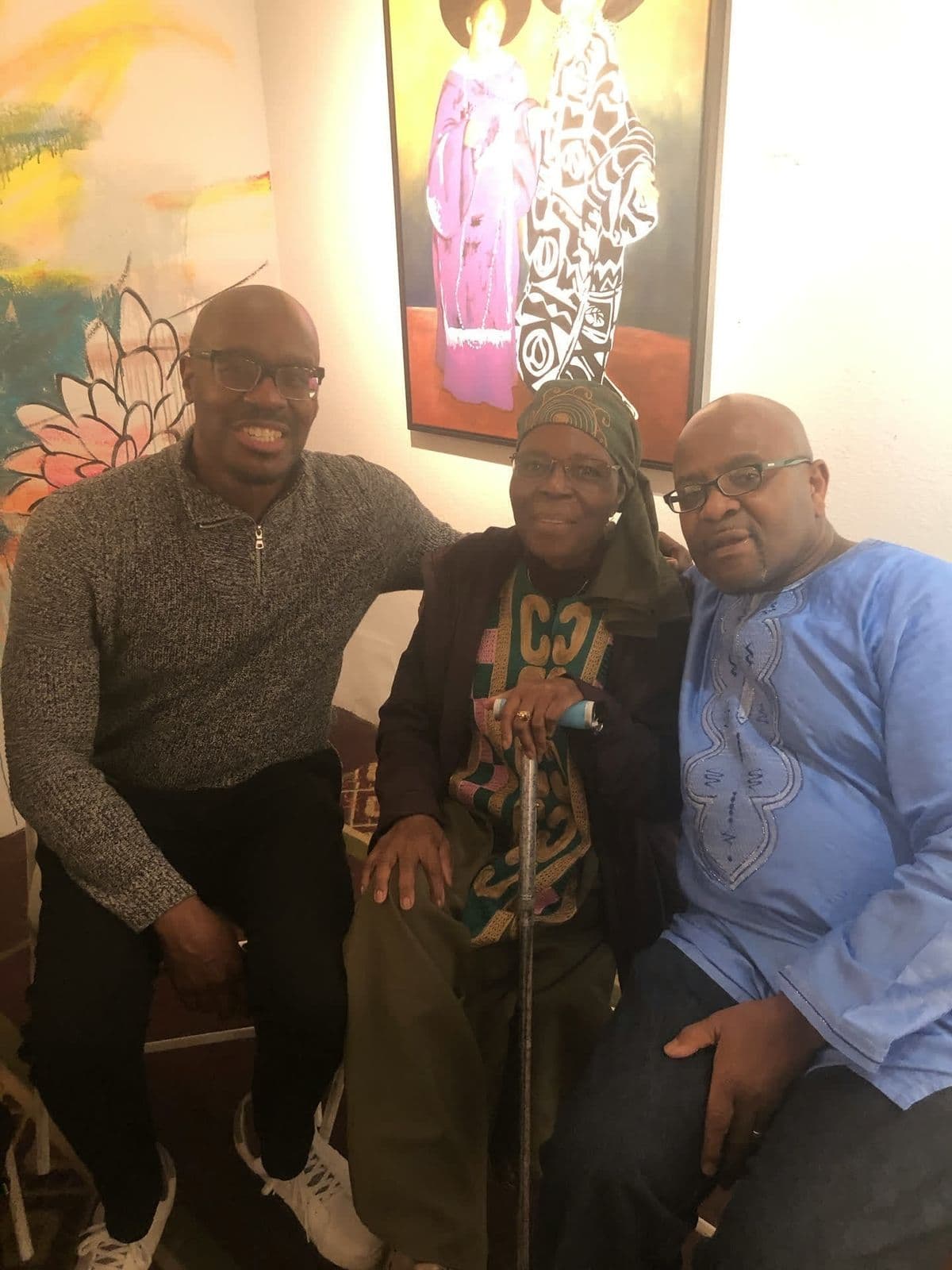 Alex with two older men, African art on the wall behind them