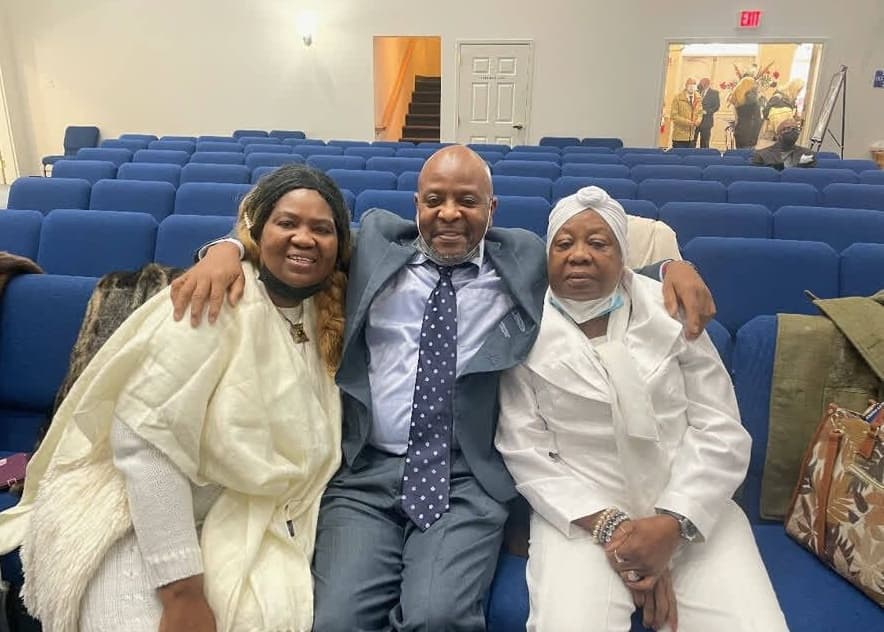 Alex seated with two women in a church, arms around both