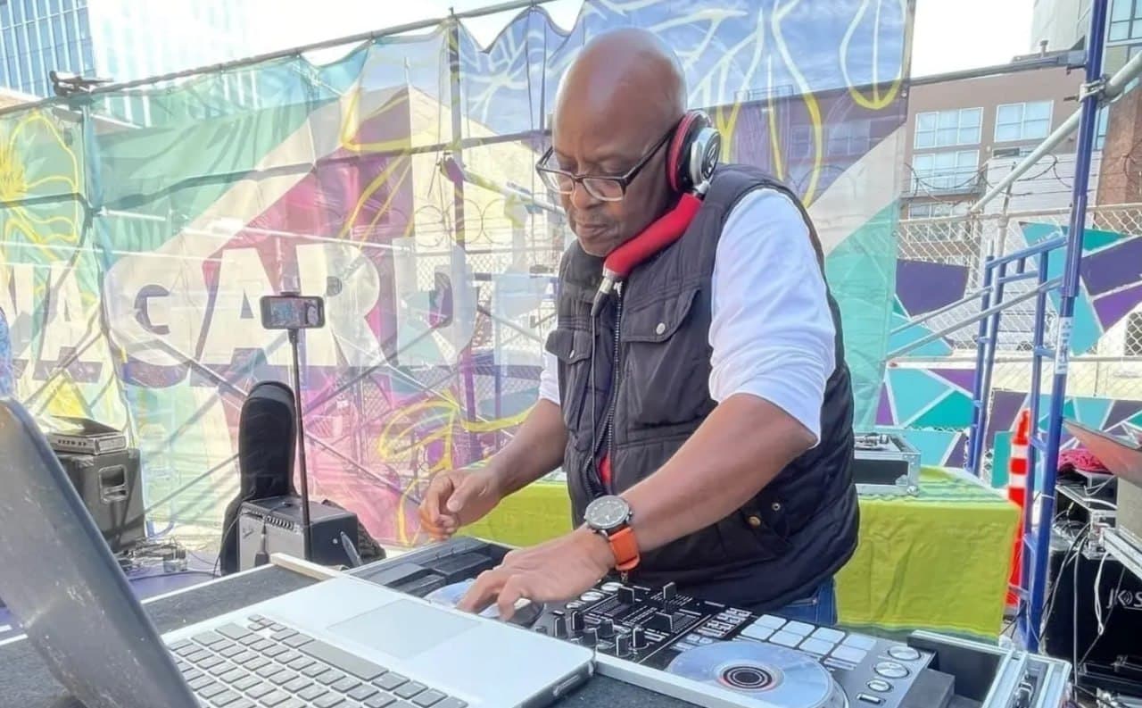 DJ Afrique DJing at an outdoor festival with colorful mural backdrop